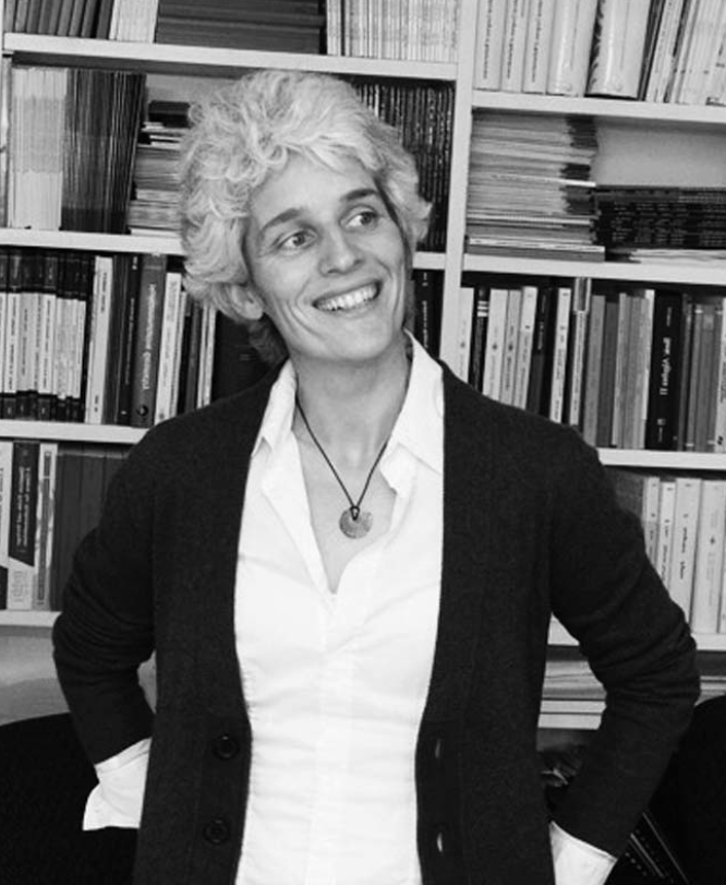 A black and white photograph of Ulrike Tillman in front of a bookcase